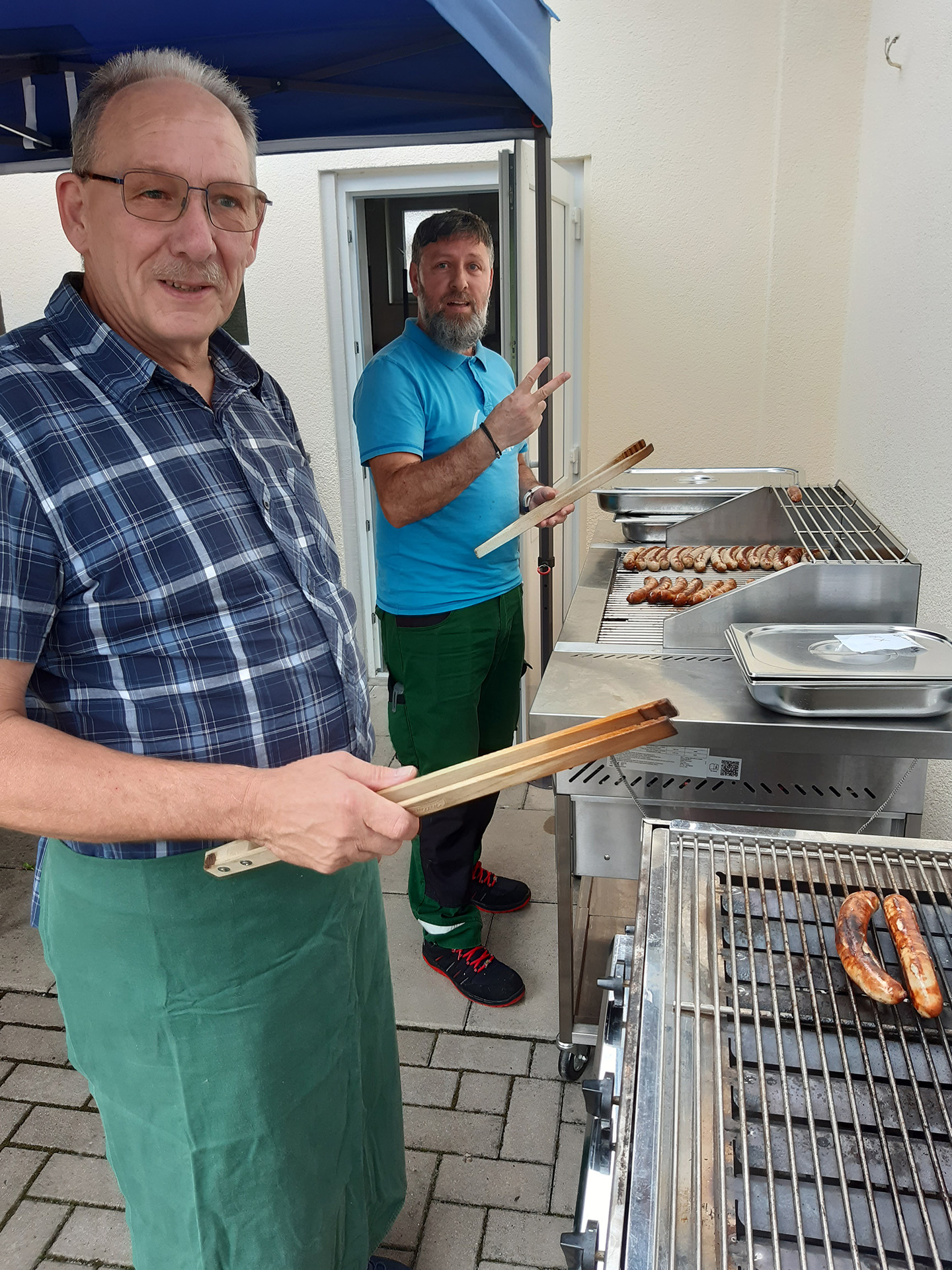 Sommerfest-Foto7 - zwei PErsonen stehen am Grill und bereiten Bratwurst zu